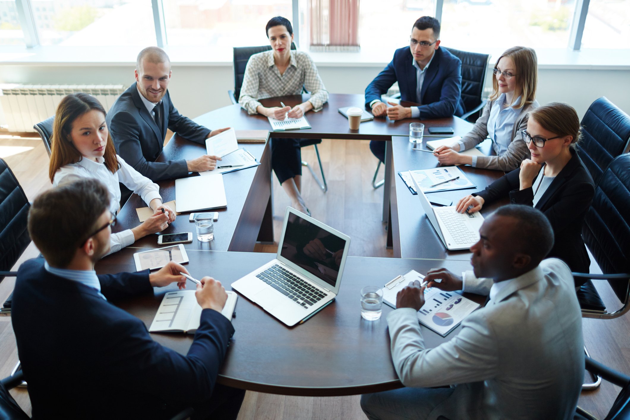 People in business attire sitting around a table in a meeting room.