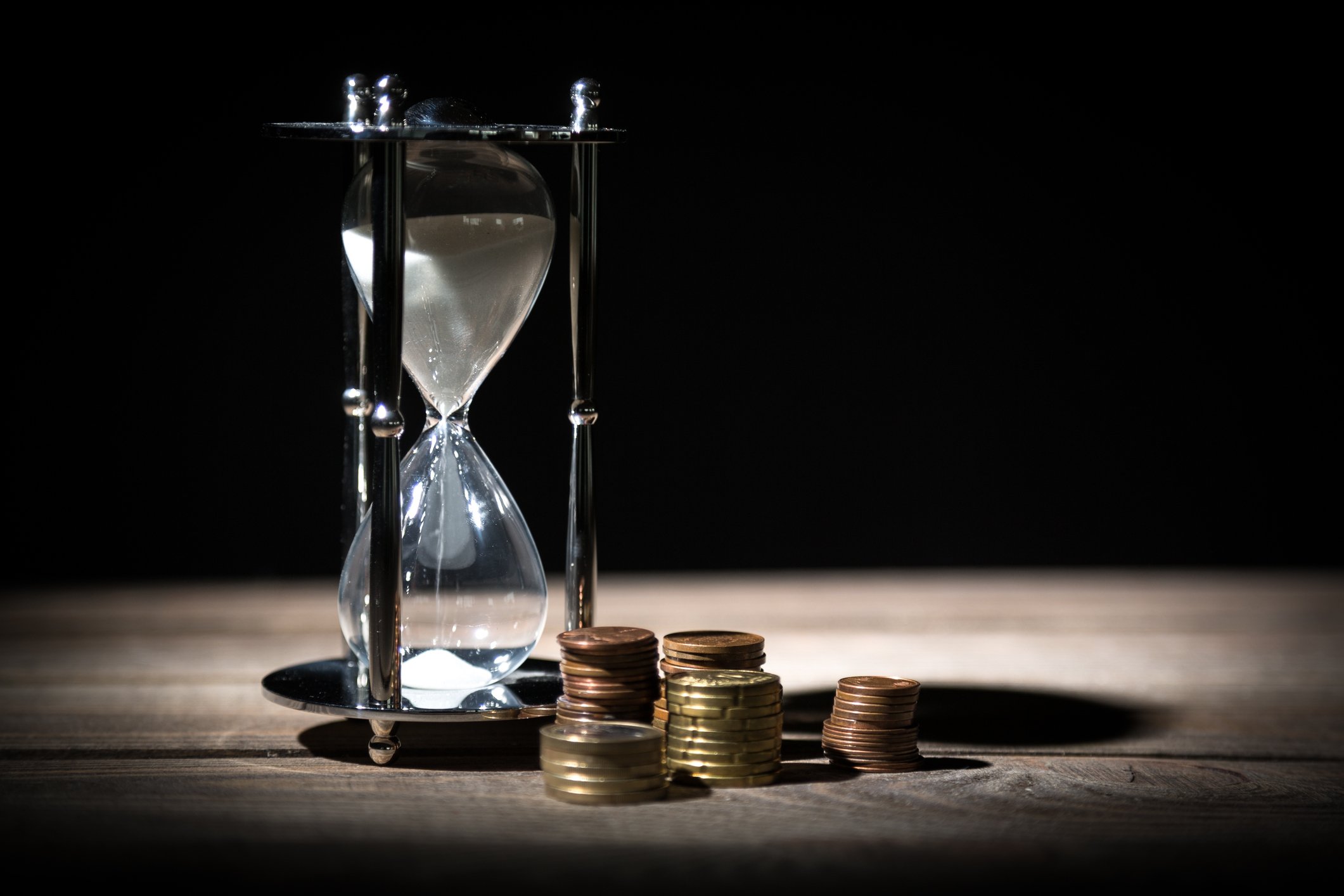 An hourglass and several stacks of coins on a table.