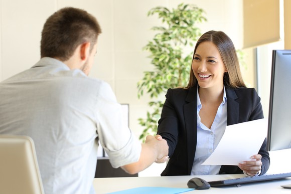 A man and a woman shake hands over a desk.