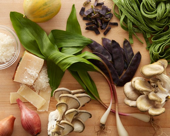 Pasta, cheese, mushrooms, and various vegetables laid out on a wooden surface.
