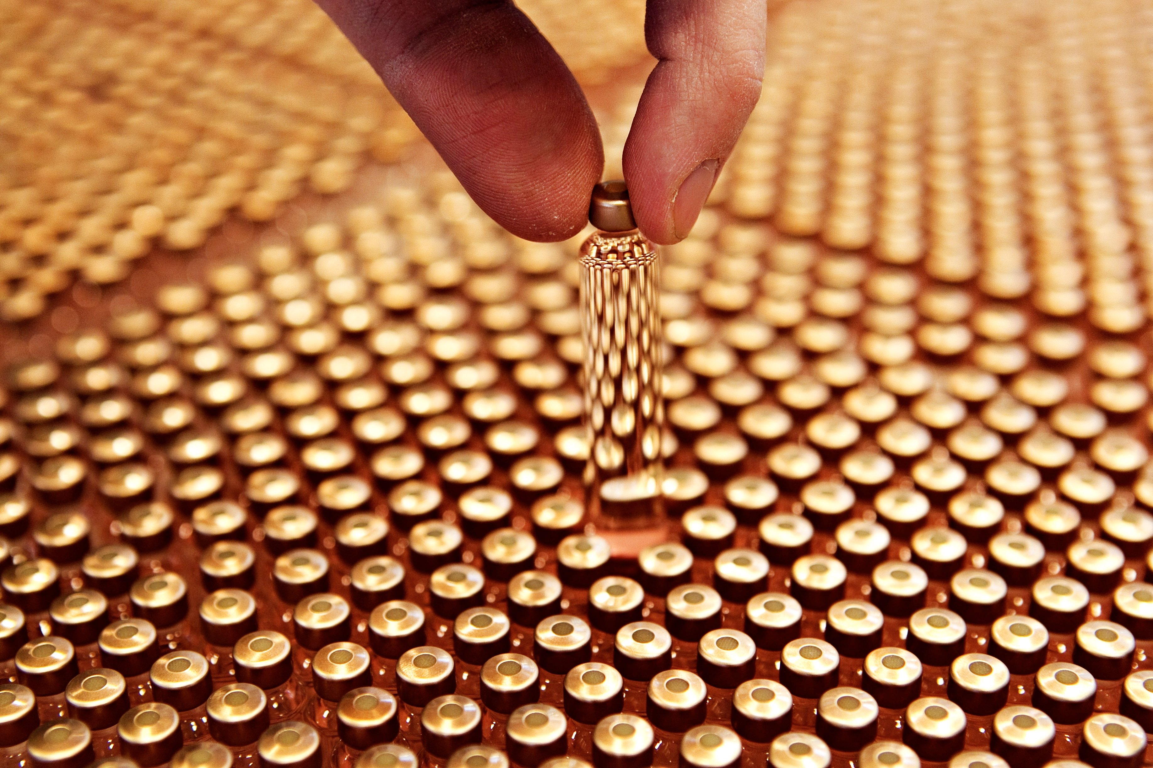 A vial of insulin held by two fingers above a tray of them