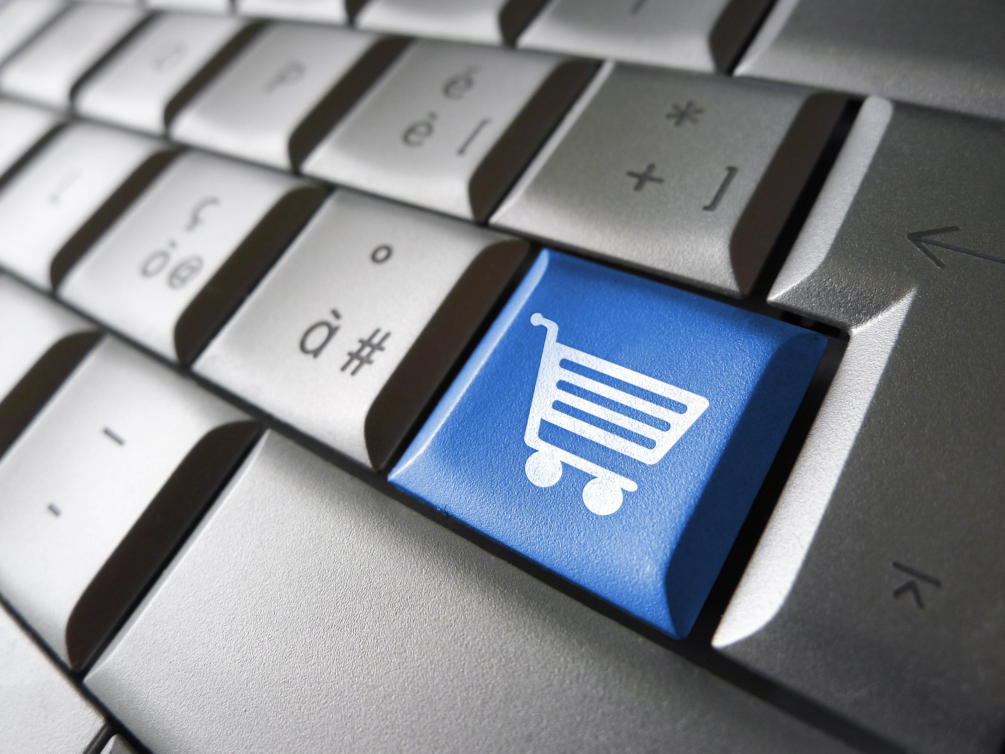 Close-up of a gray computer keyboard with one bright, blue key featuring a white shopping cart icon.