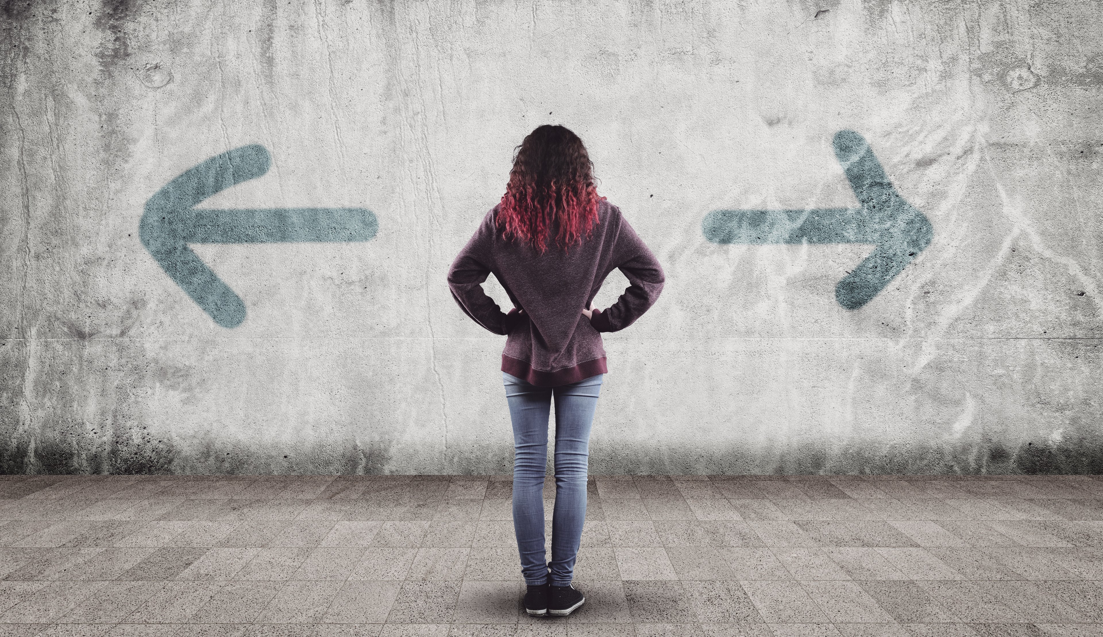 A woman looking at a wall with two arrows pointing in two opposite directions.