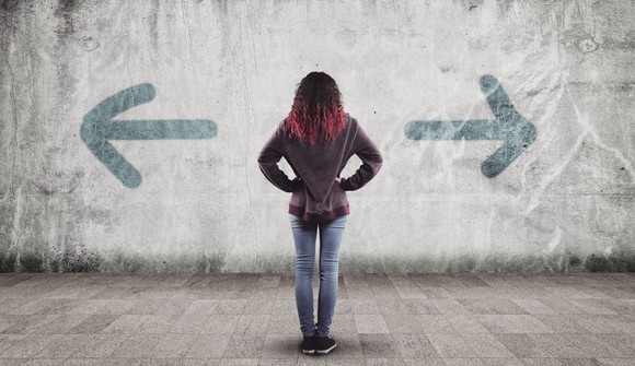 A woman looking at a wall with two arrows pointing in two opposite directions.
