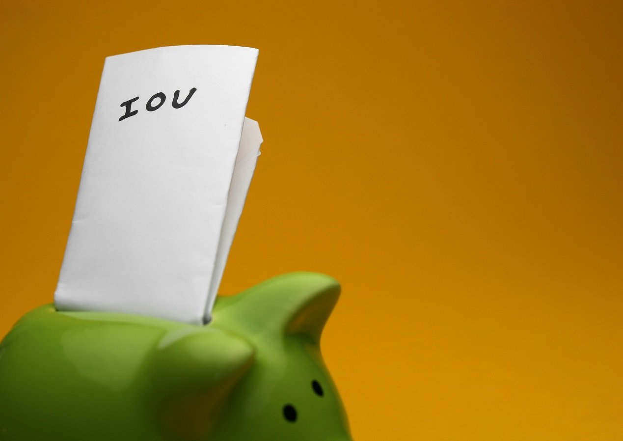 A folded piece of paper marked "IOU" protrudes from the slot of a green piggy bank.