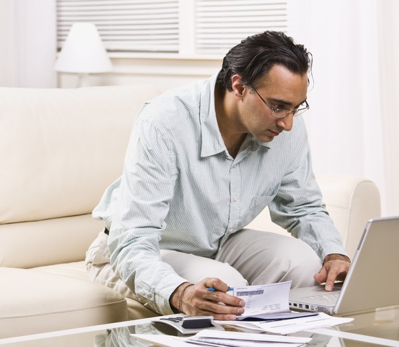 Man holding checkbook and looking at laptop.