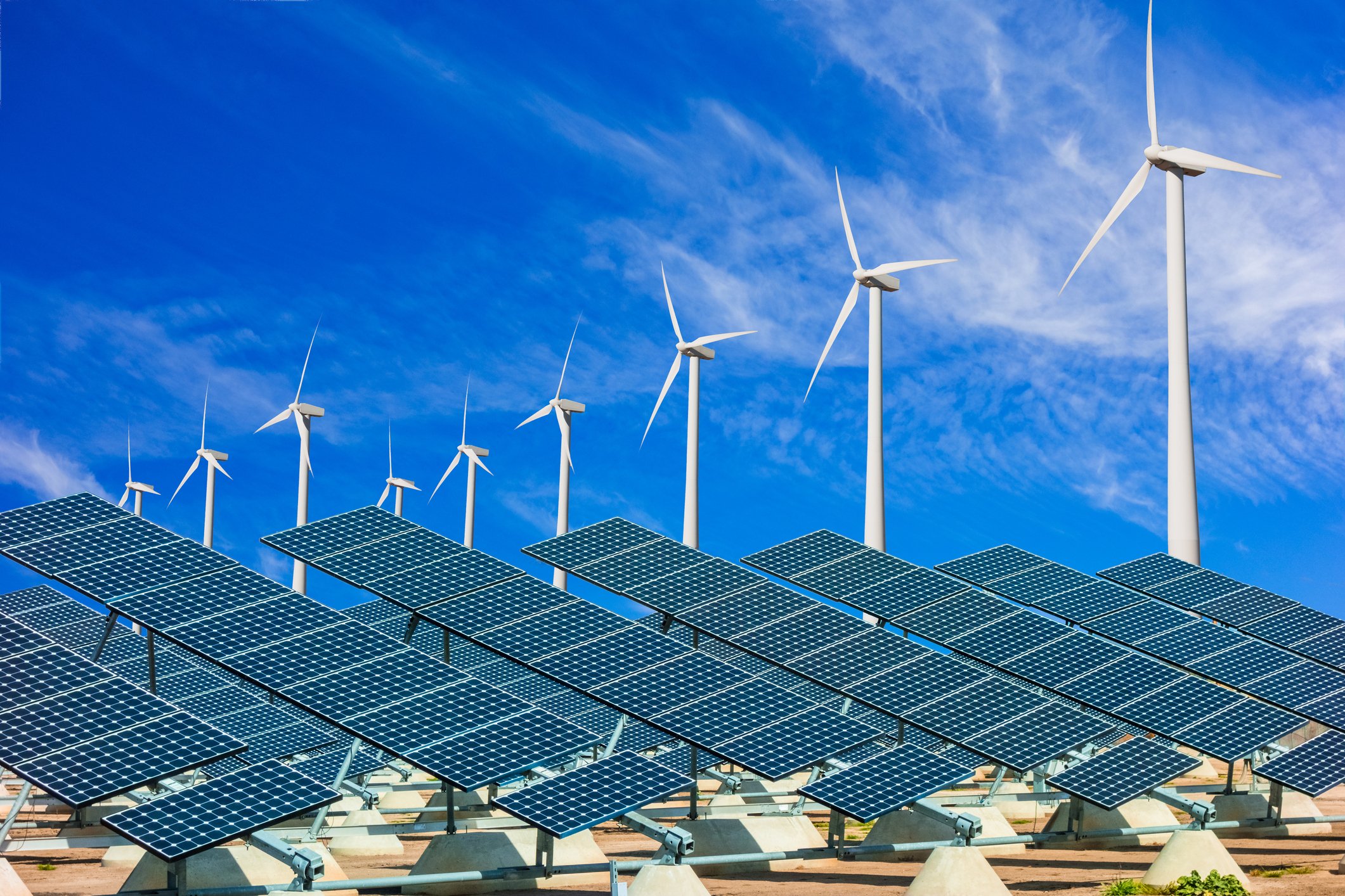 Solar panels with wind turbines in the background on a sunny day.