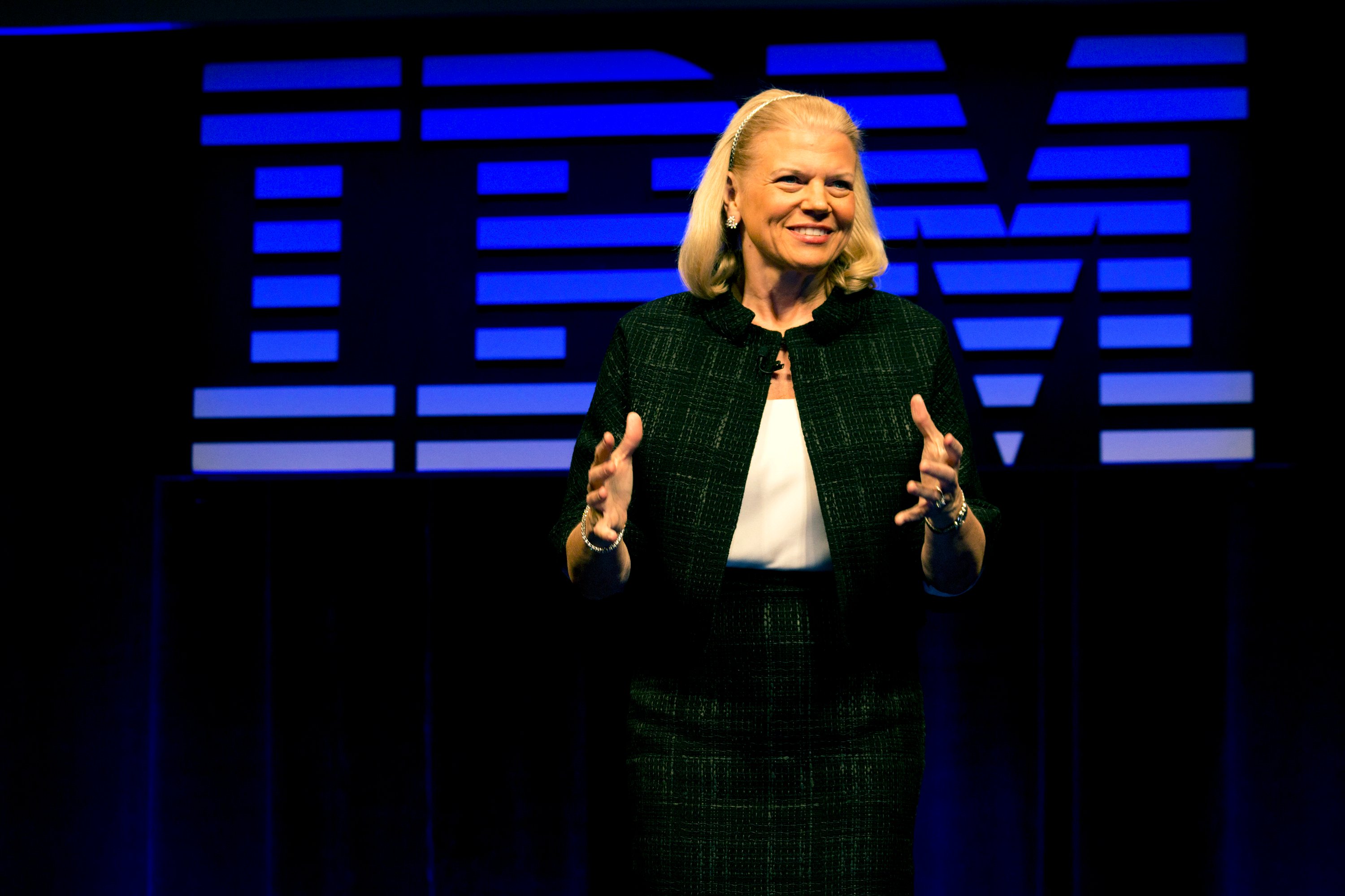 Ginni Rometty speaking at an IBM event, with the logo large behind her