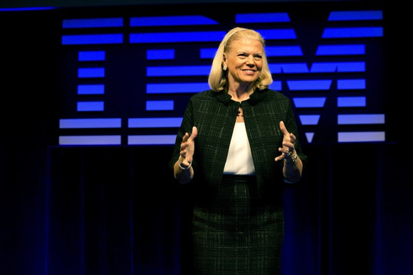 Ginni Rometty speaking at an IBM event, with the logo large behind her