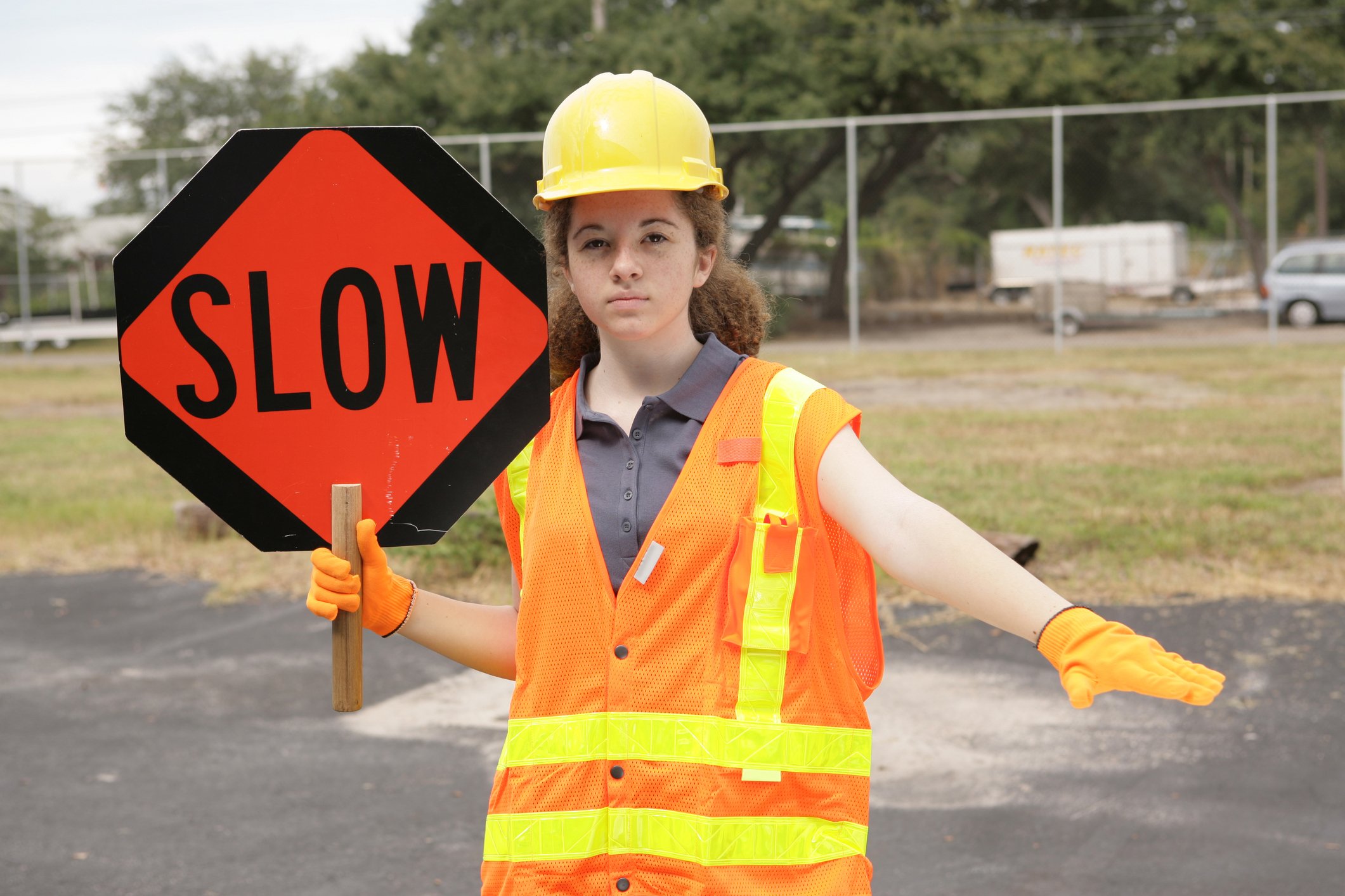 A female traffic guard holding a sign that says "SLOW" and signaling with her hand to slow down