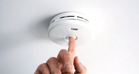 A person using their finger to test an in-home smoke alarm. 