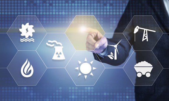 A businessman touching a screen displaying icons for various energy industries, such as oil drilling and nuclear power.