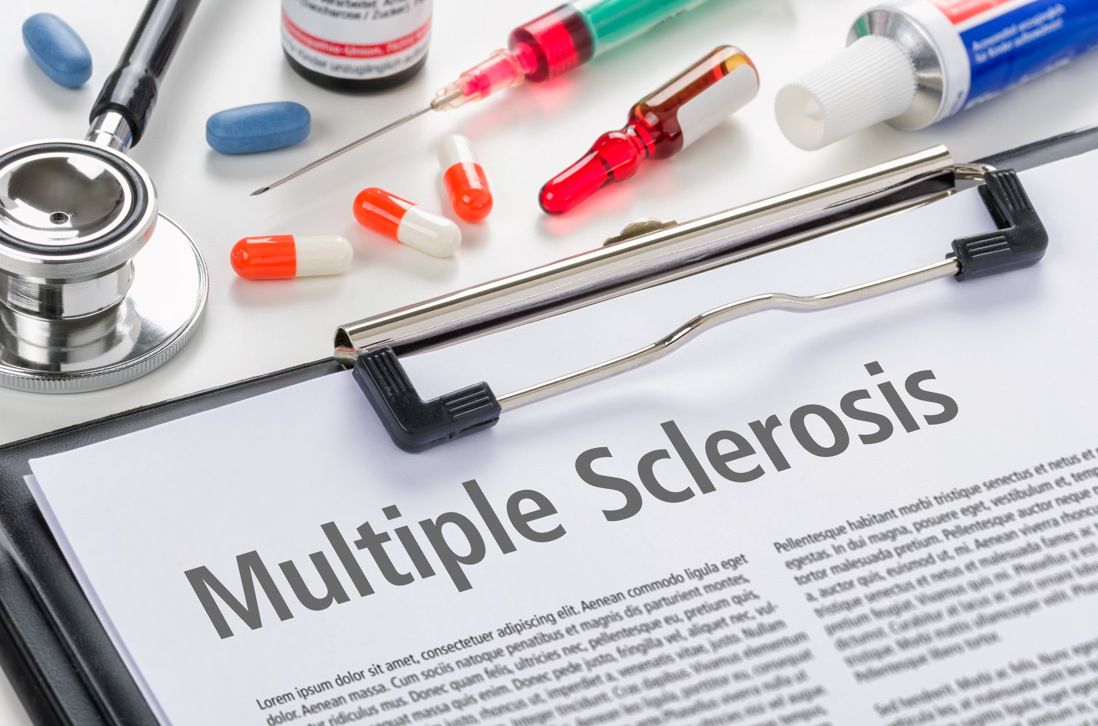 Paper on clipboard with heading of "multiple sclerosis" next to stethoscope, syringe, and pills