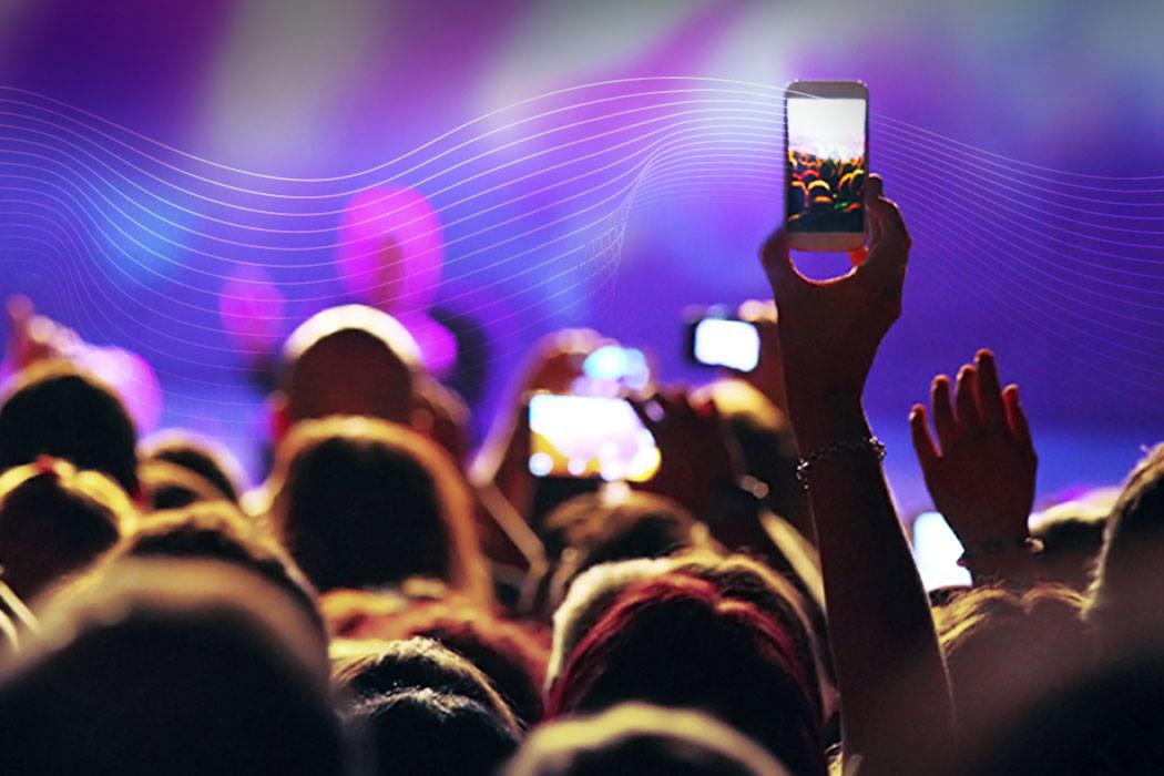 Person in a crowd, holding up a smartphone to take a picture.