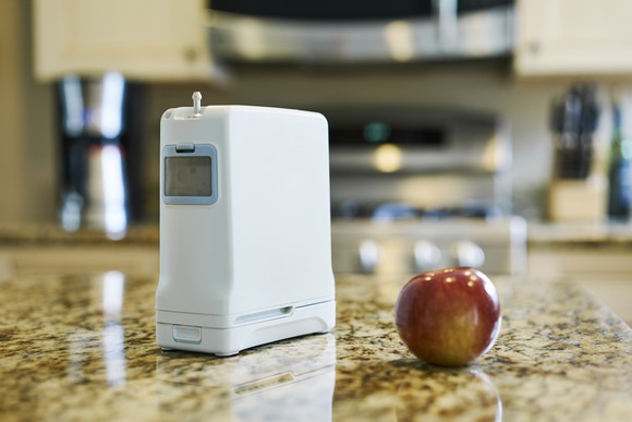 Inogen G4 next to apple on a table. 