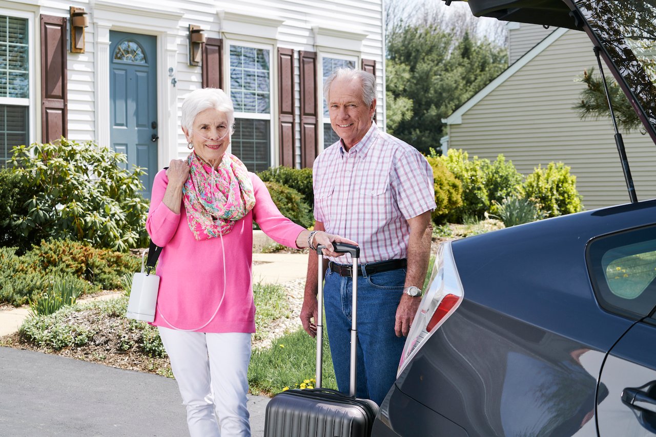 older woman and man holding Inogen product near car