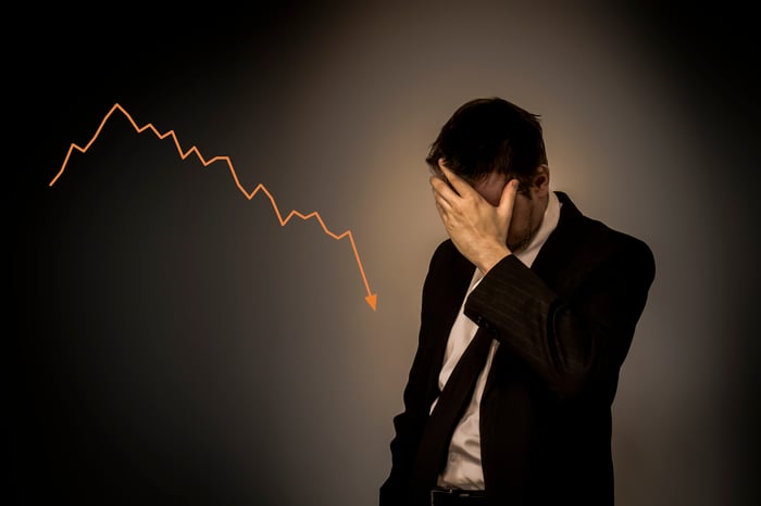 Man holding his forehead and standing in front of a downward-trending chart.