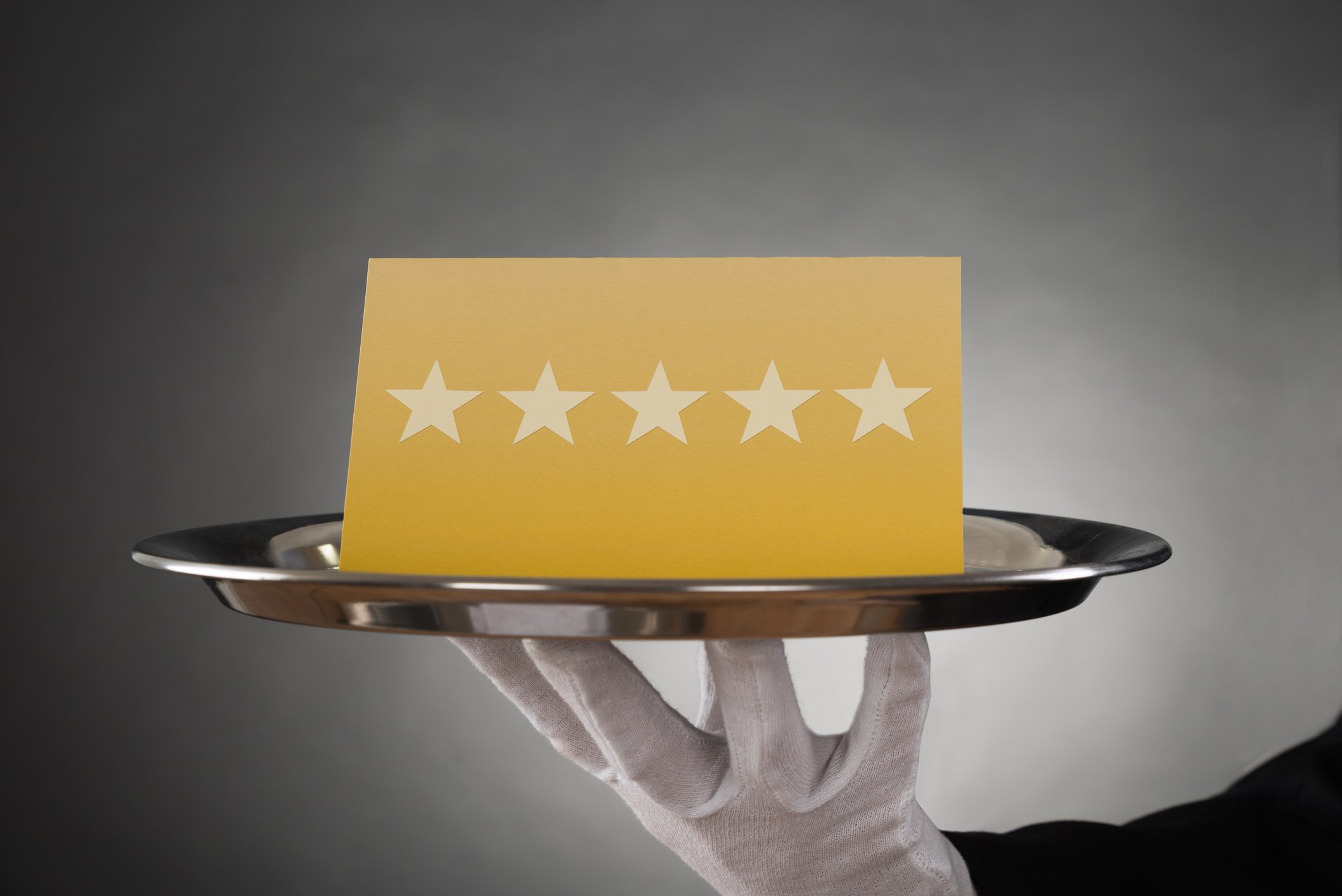 A butler holds a tray with a card displaying five stars in a row.