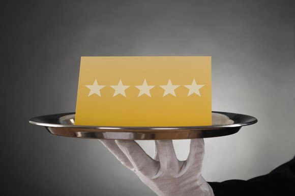 A butler holds a tray with a card displaying five stars in a row.