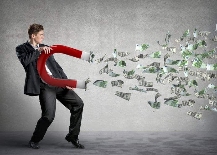 Man wearing suit holding giant red magnet with cash flowing toward the magnet