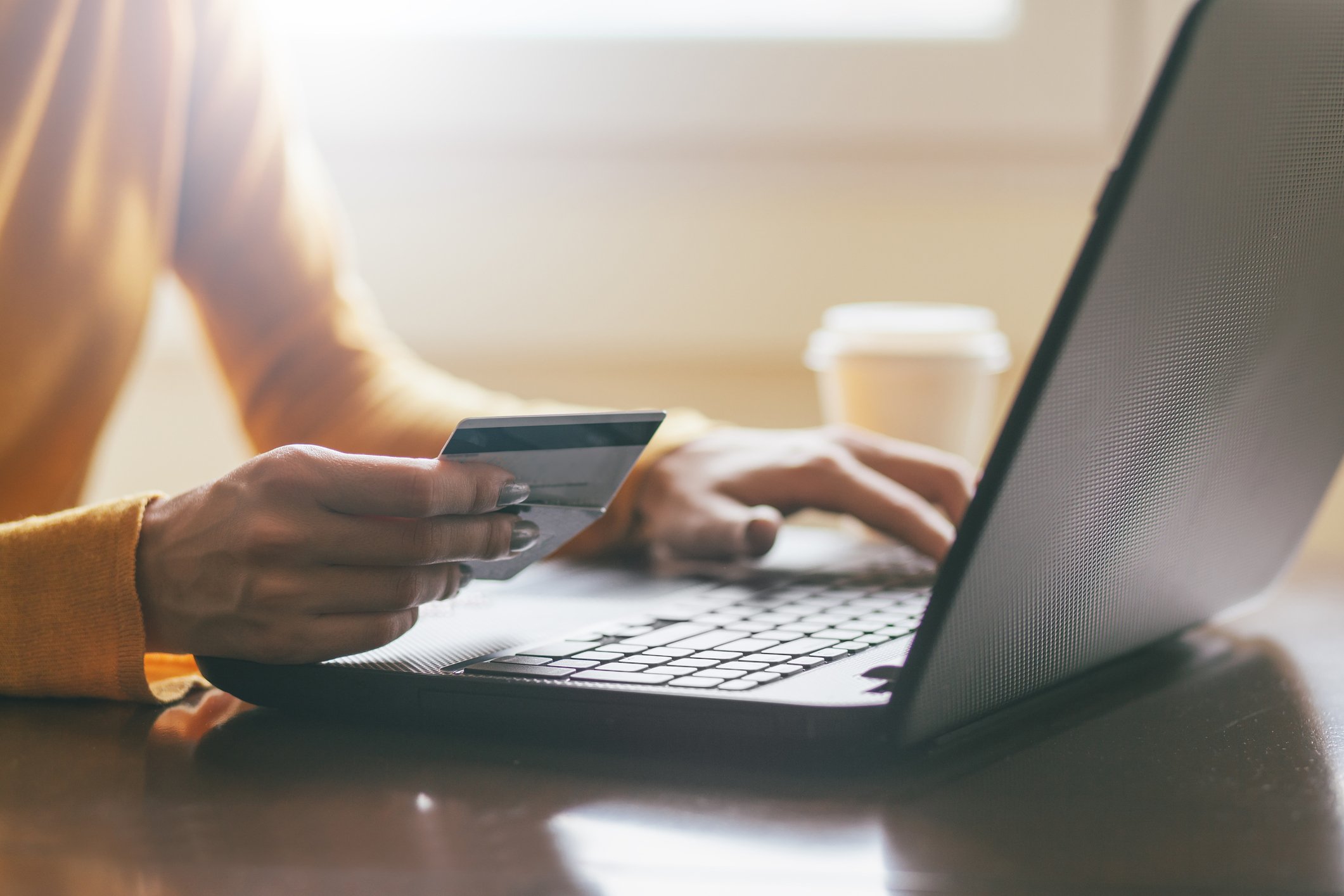 Woman holding credit card in one hand while typing with the other on a laptop.