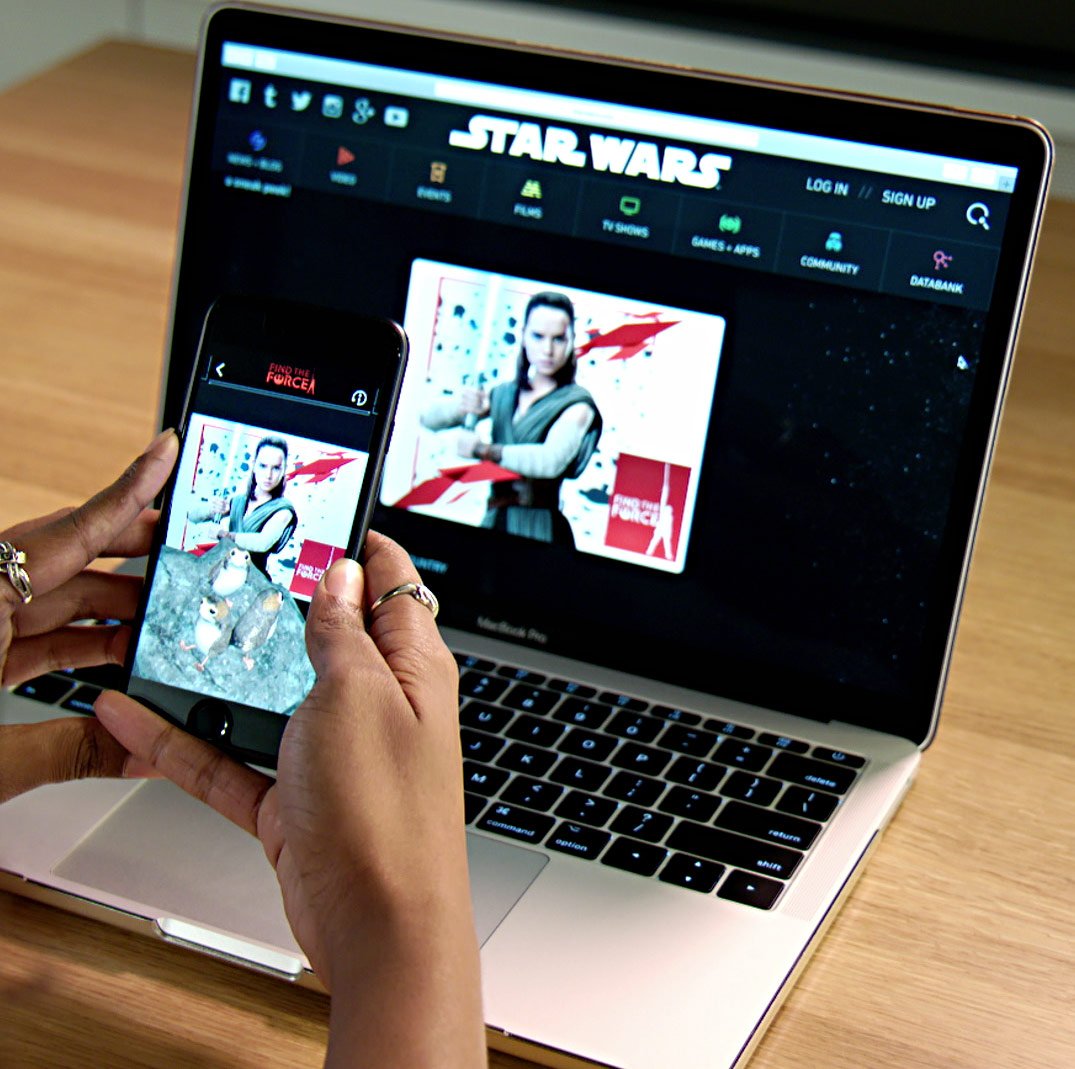 A person using the Disney Find the Force app on their smartphone in front of a laptop