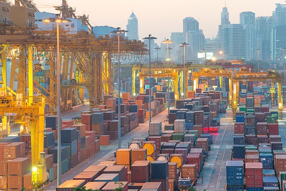 Containers at commercial port of Bangkok with city buildings in the background.