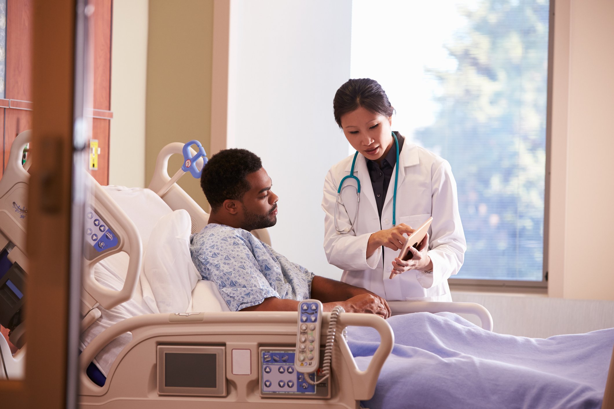 A female physician consulting with a male patient in his hospital bed.