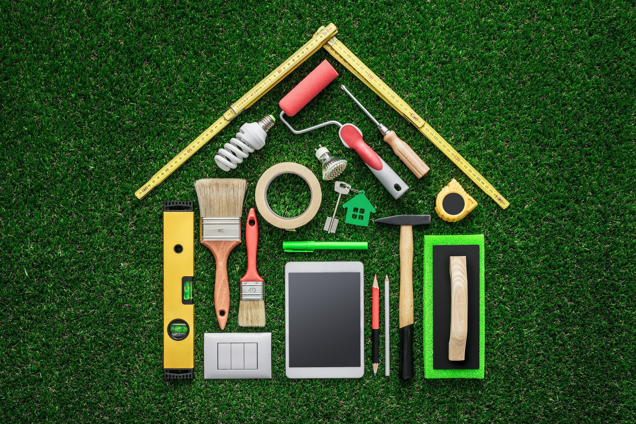 Common tools and supplies laid out on green artificial turf in shape of a house.