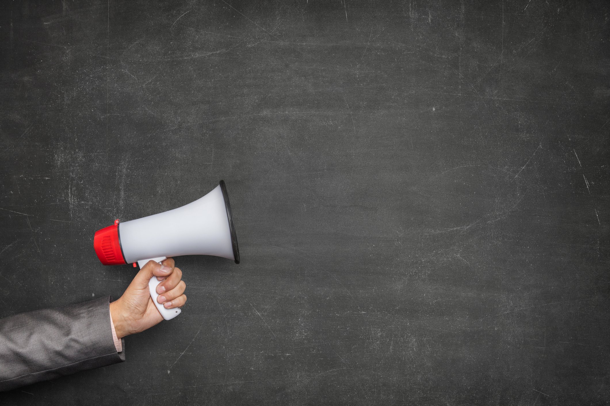 A person's arm holding a megaphone with a chalkboard background behind it.