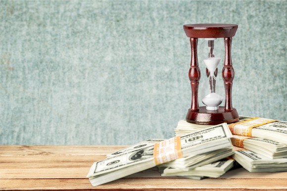 Piles of money stacked up near a sand timer