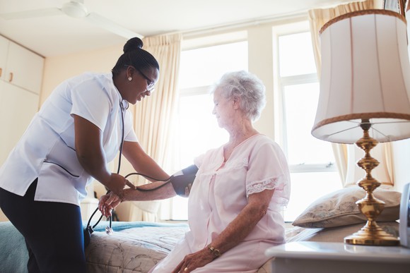 A female healthcare worker takes a female senior patient's blood pressure.