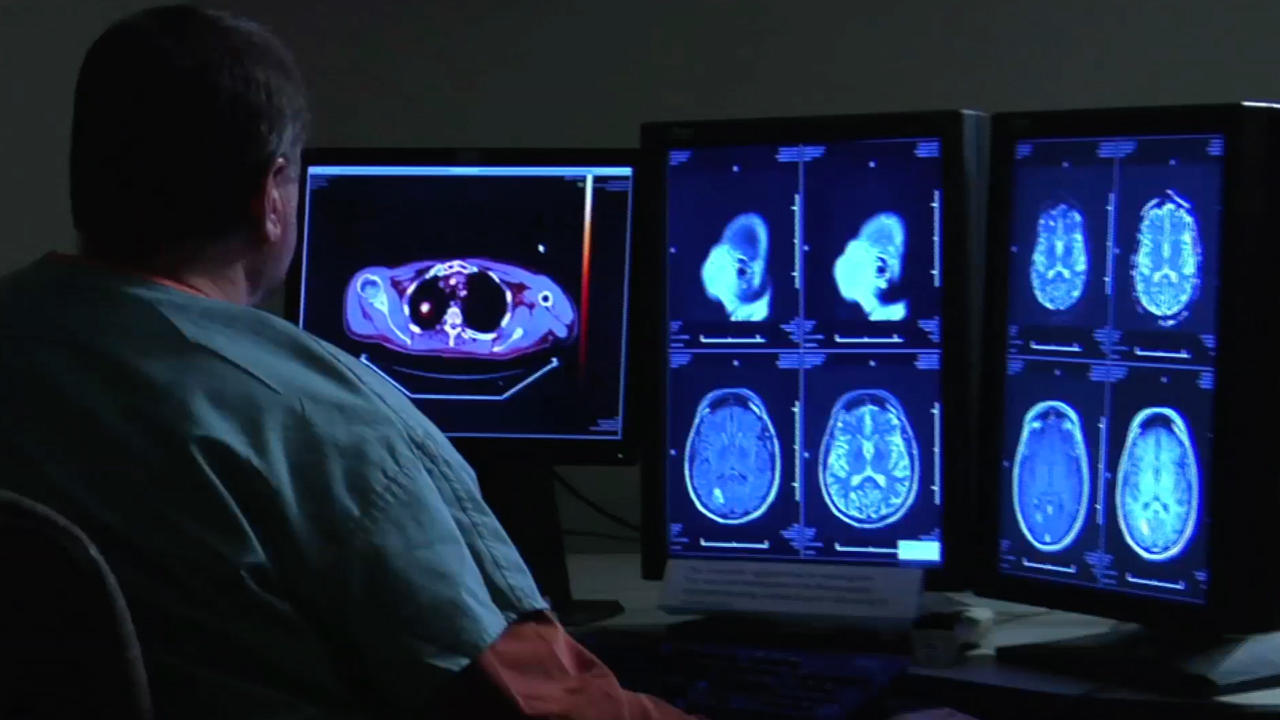 Man in scrubs sitting in front of monitors showing medical images