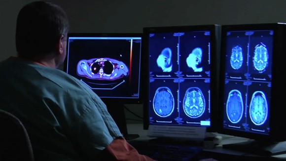Man in scrubs sitting in front of monitors showing medical images