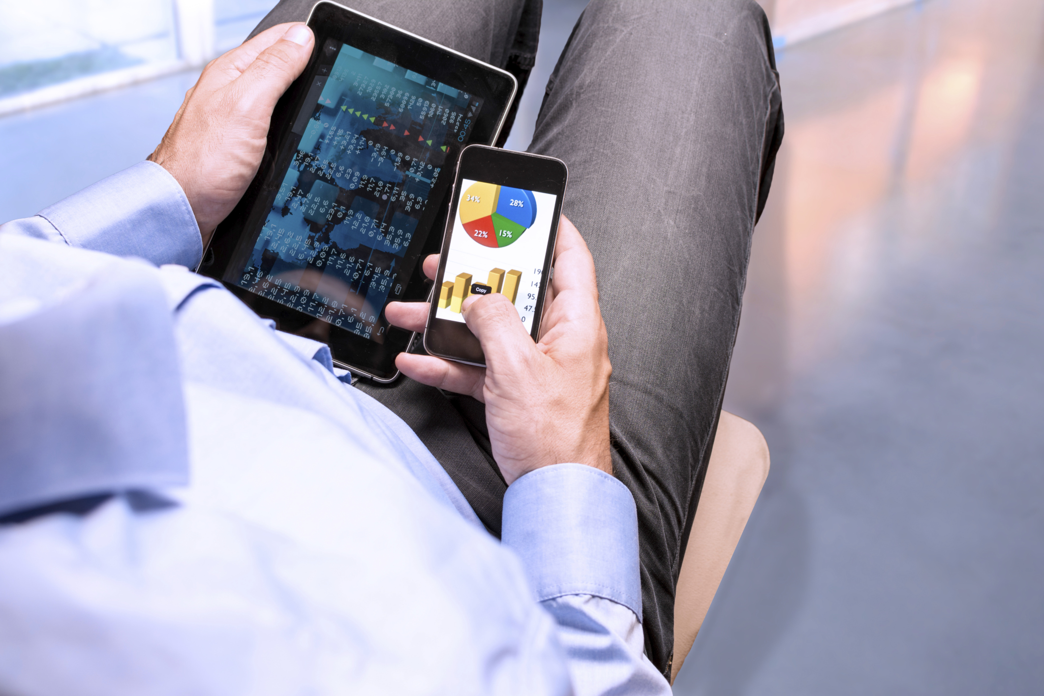 Man holding a tablet and smartphone in his lap.