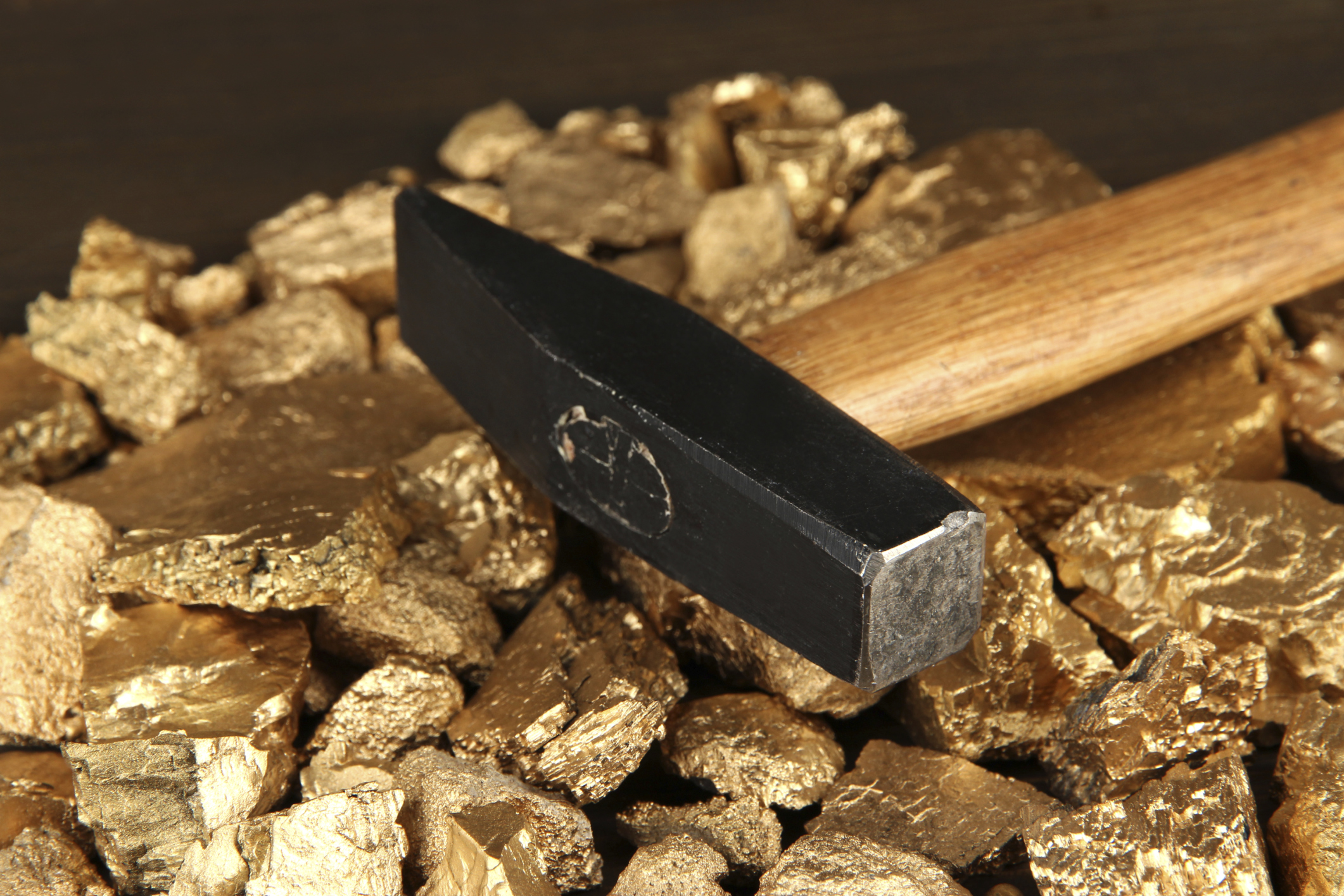 A rock hammer lying atop gold nuggets.