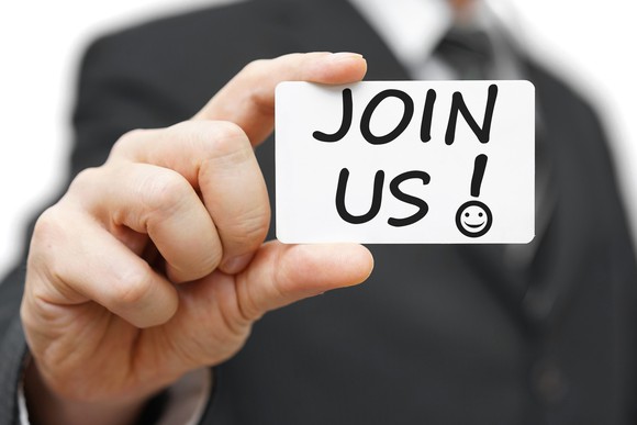 A man holds up a card that says, "Join us!"