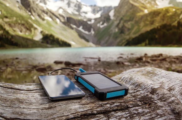 A phone sits next to a solar charger overlooking a mountain.