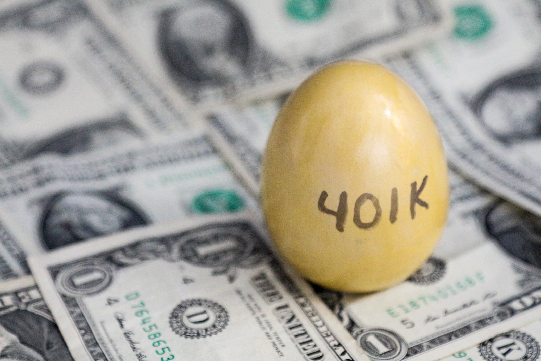 A golden egg with the word "401k" written on it, lying on a pile of cash.