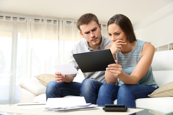 Couple looking at tablet PC with worried expressions.