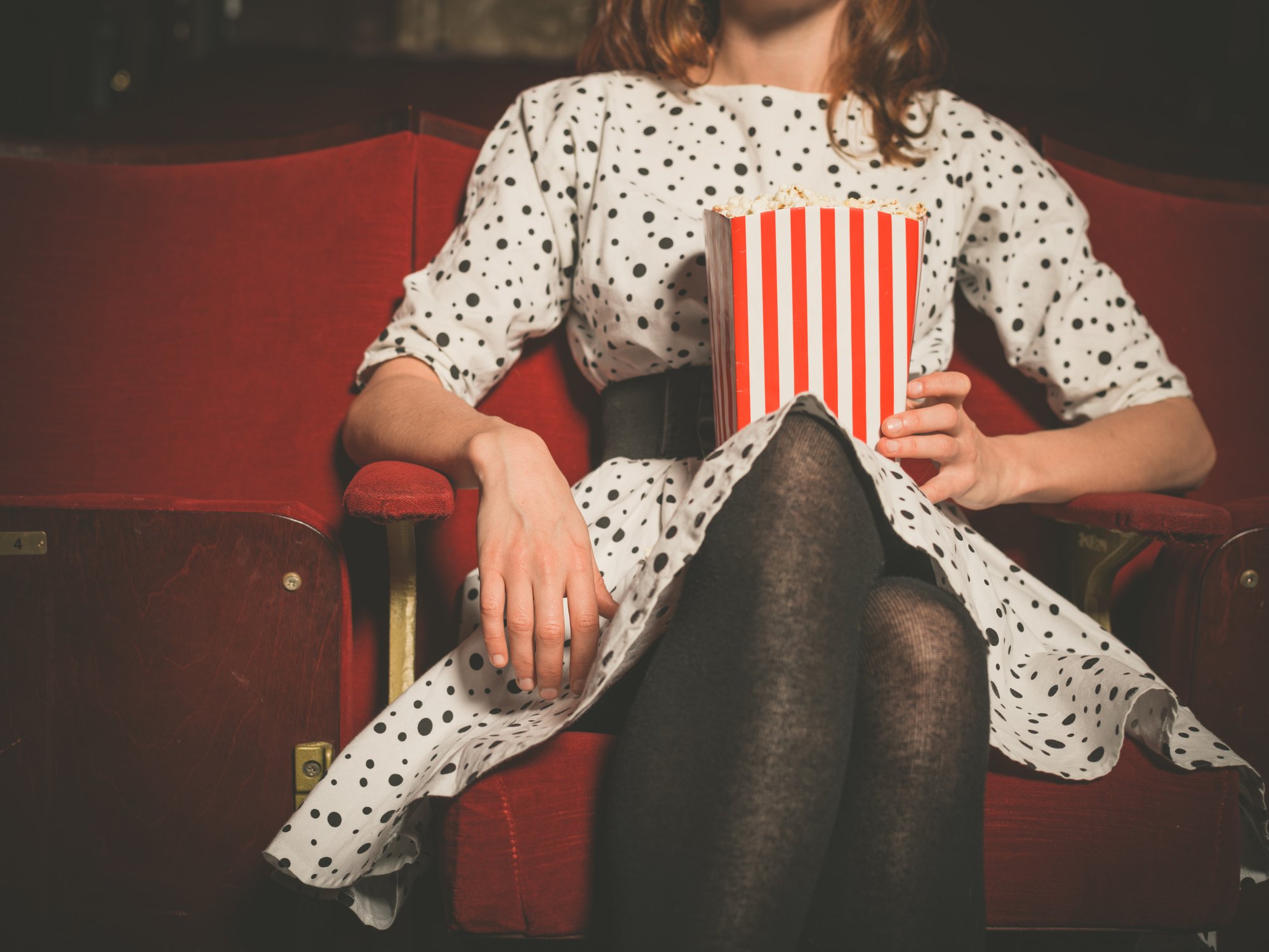 A woman sitting in a theater holding a red and white striped bag