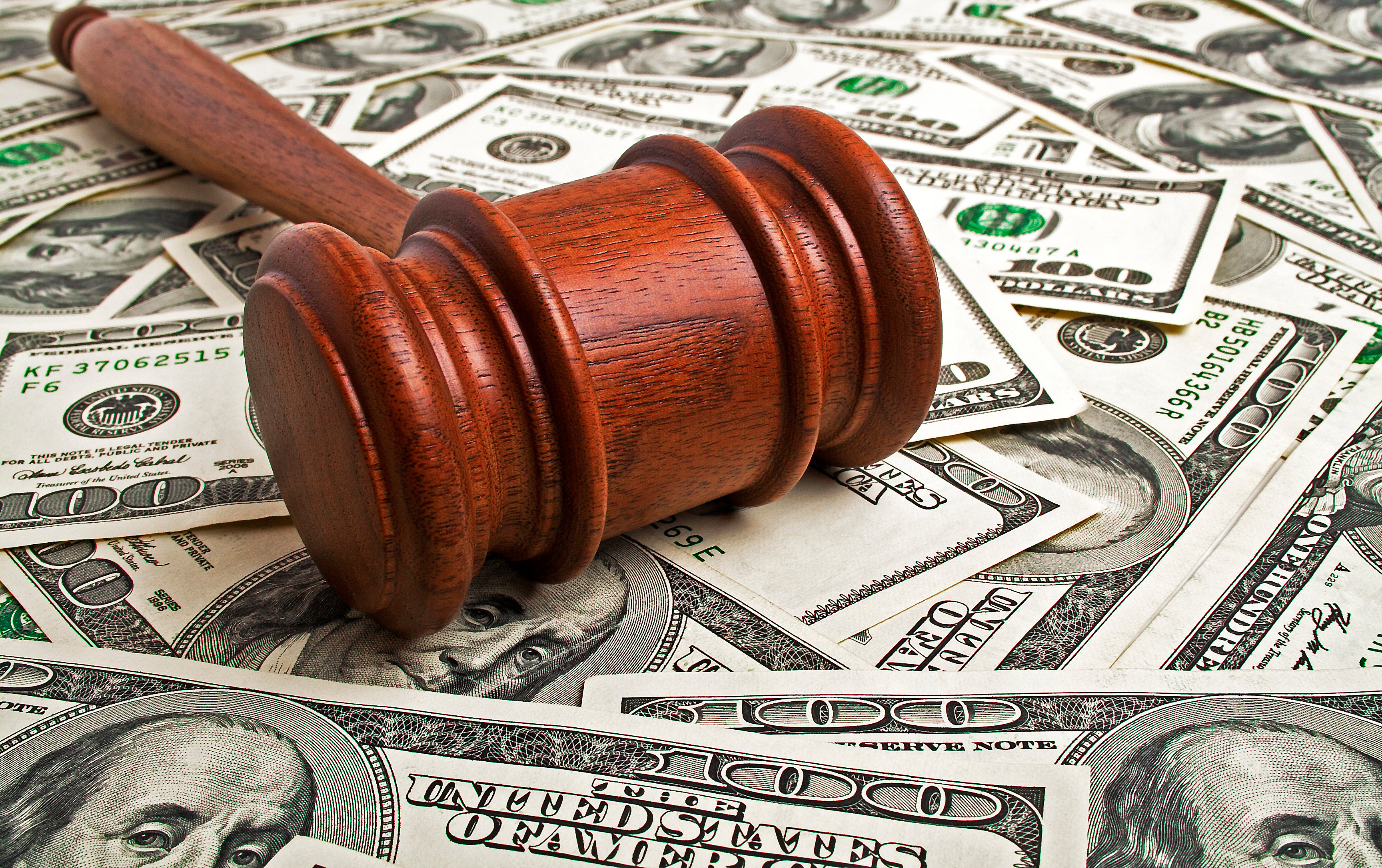 A wooden gavel rests atop a pile of money.
