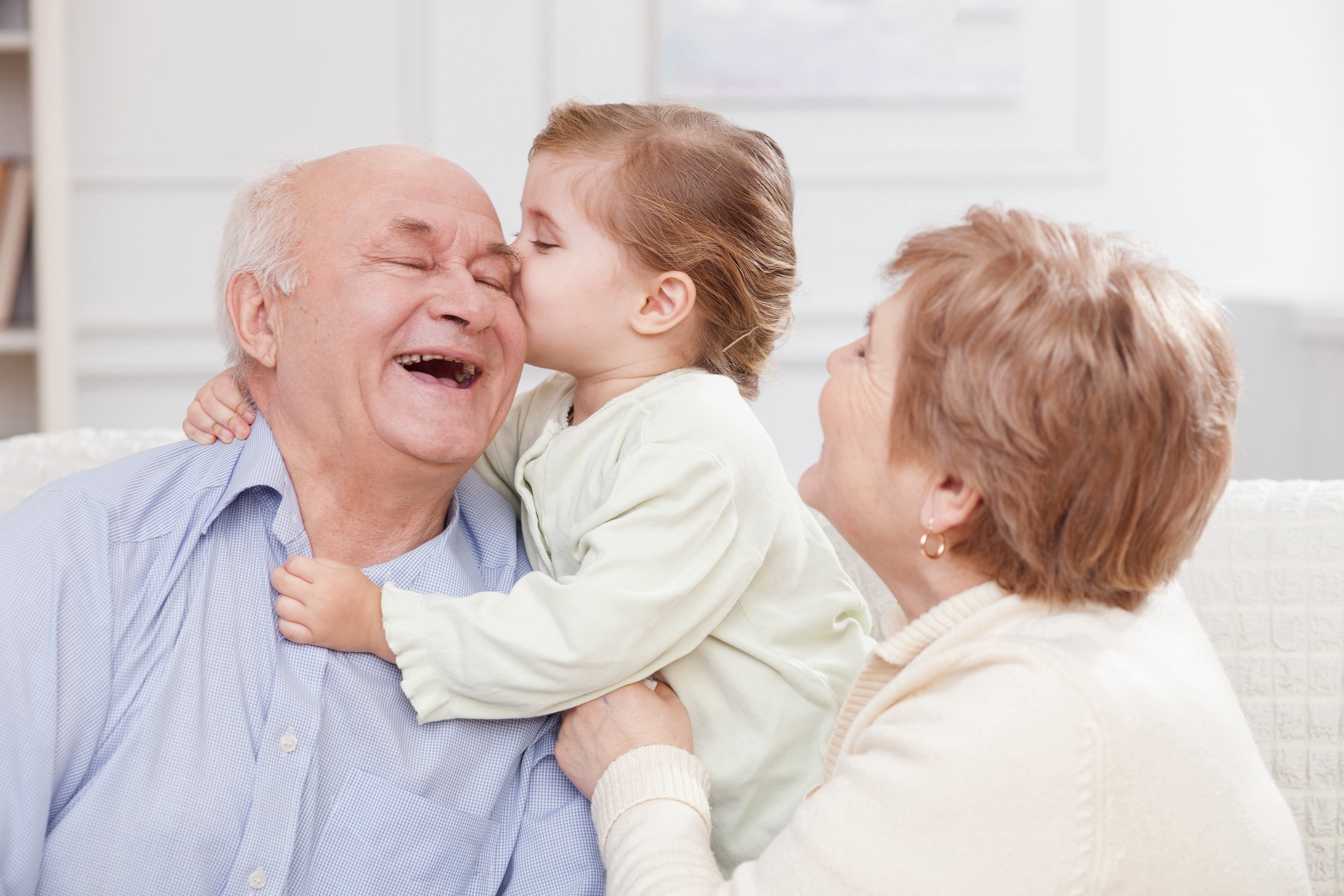 Young child kissing elderly male on forehead while elderly female looks on.