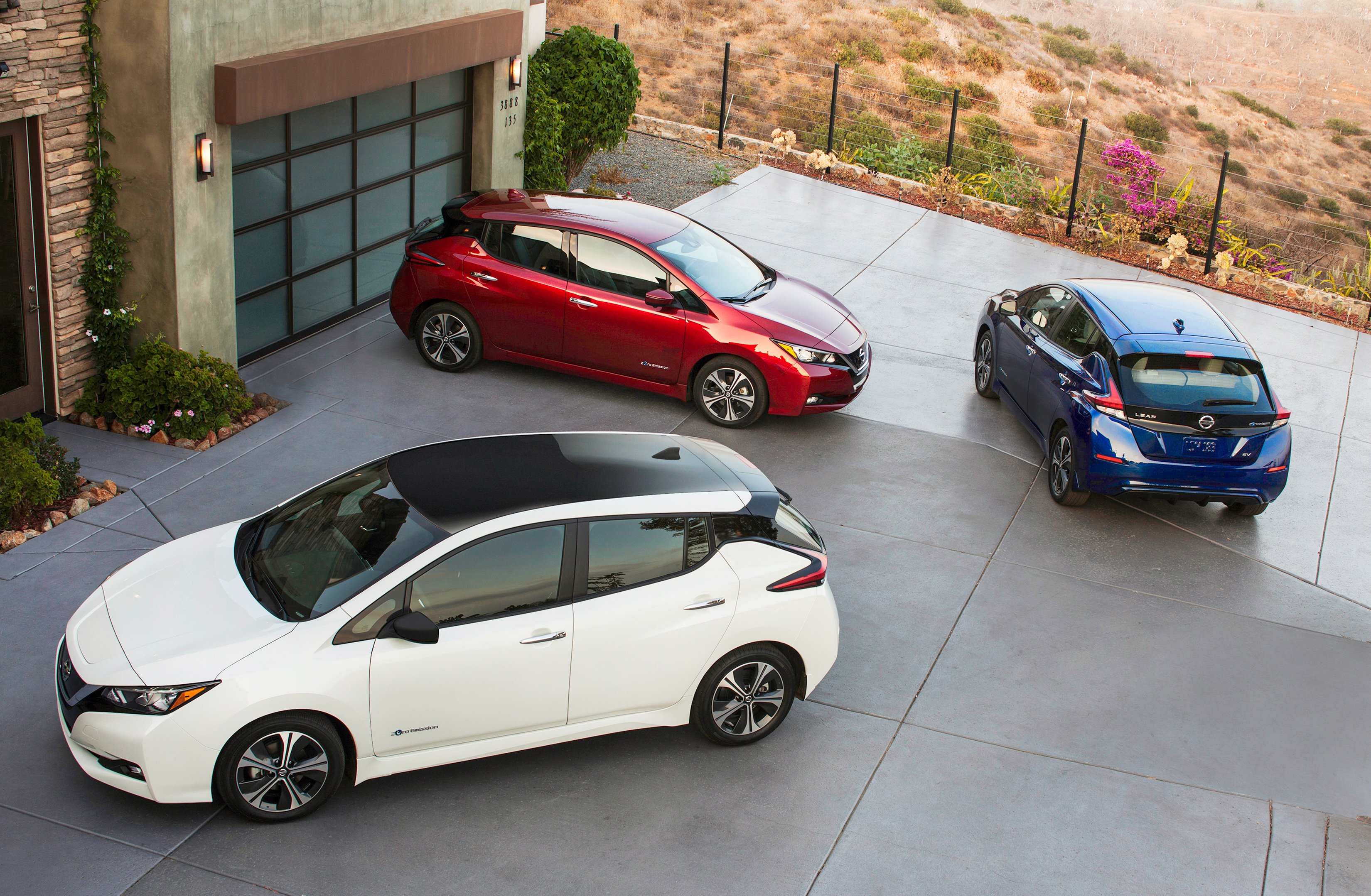 Three 2018 Nissan Leafs -- red, white, and blue -- in a suburban driveway.