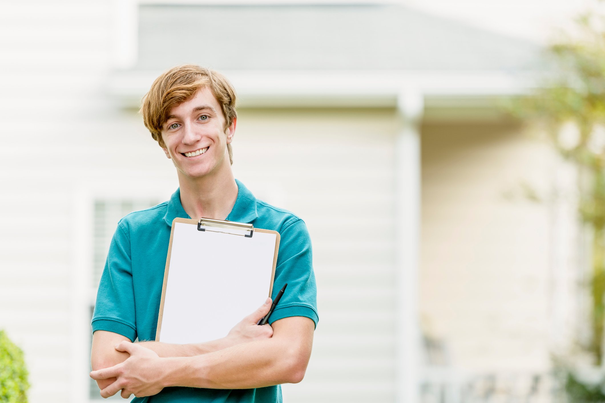 A smiling man stands outside a house, clutching a clipboard.