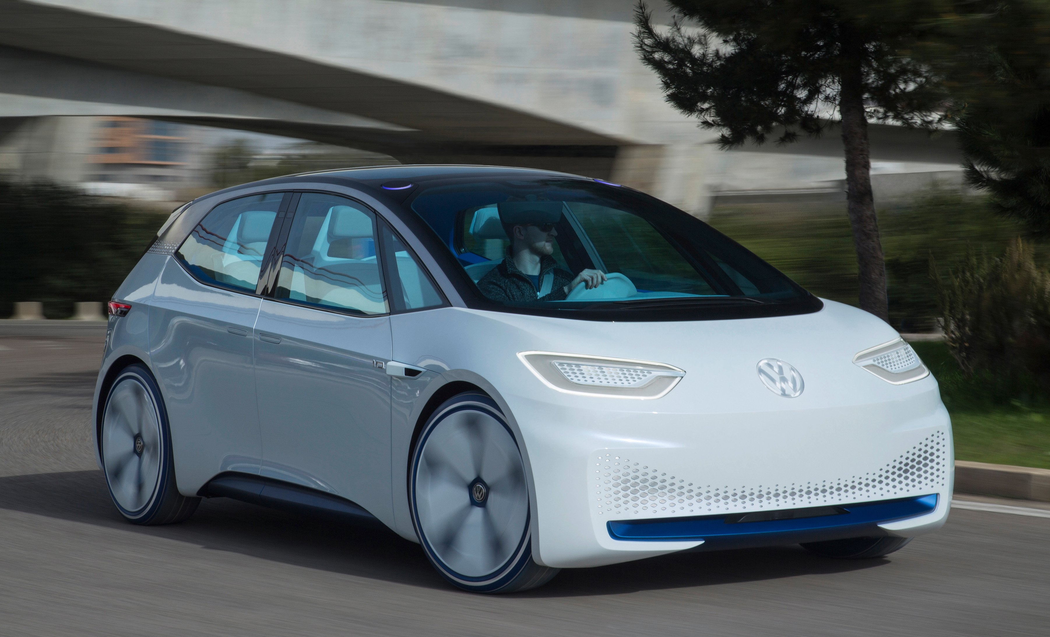 The Volkswagen I.D. Concept, a futuristic-looking white hatchback with a black roof, on a road.