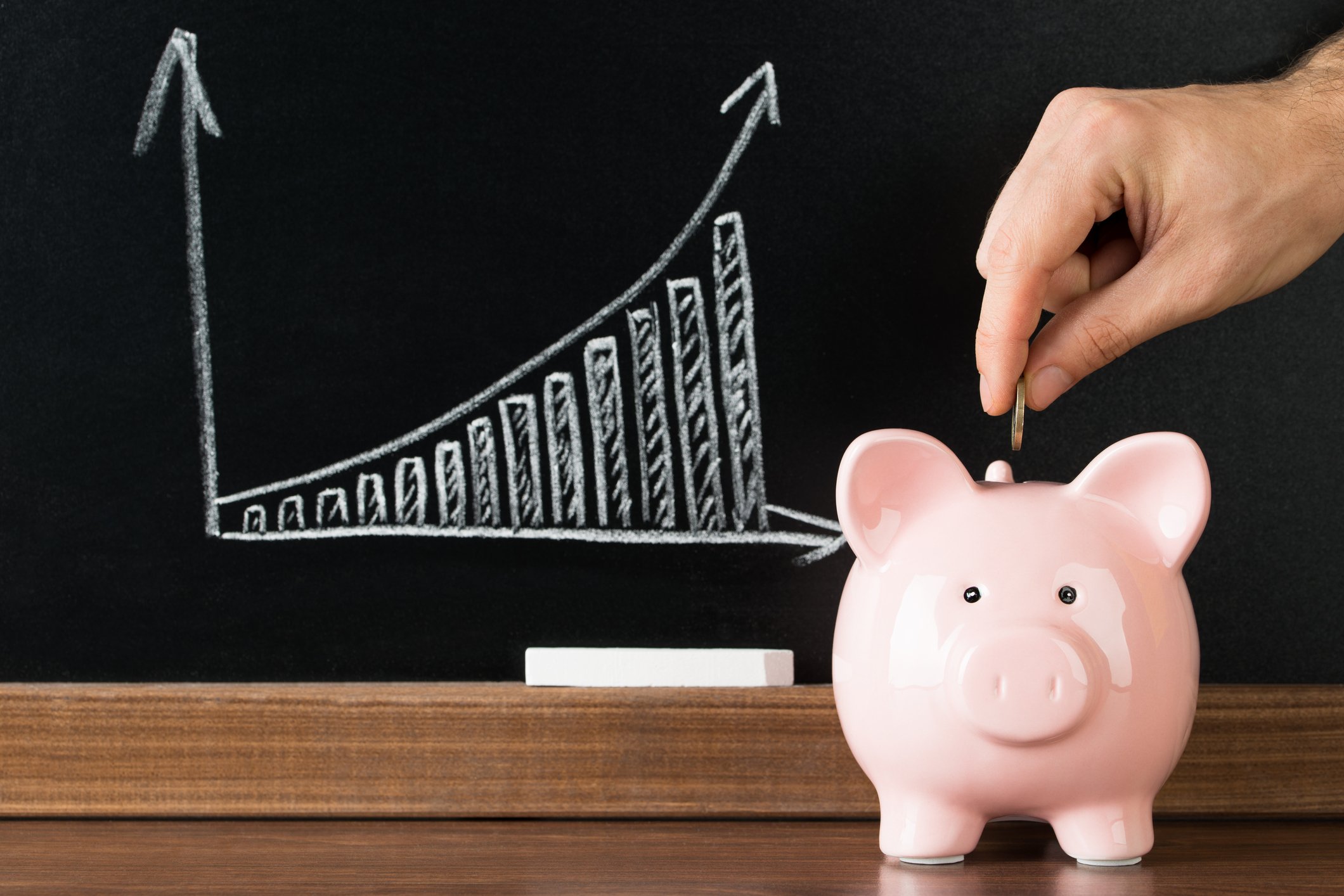 Man putting a coin in a piggy bank with a chart of growing value over time in the background.
