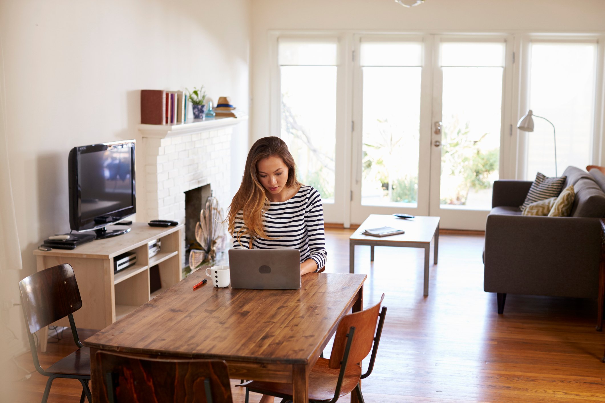 A woman sits at a table in her home, working on a laptop.