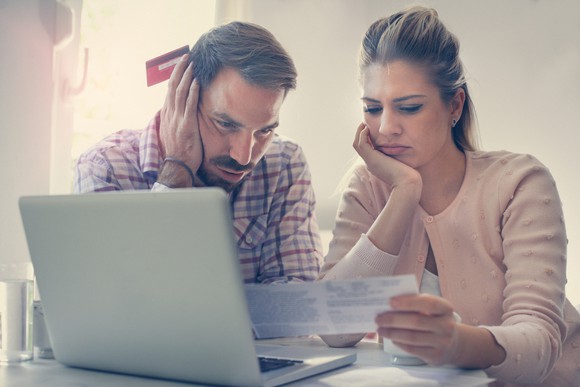 A couple, sitting side by side in front of an open laptop, show concerned  expressions as they review a document.
