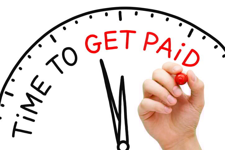 Hand writing the words "Time To Get Paid" with red marker on the drawing of a clock on a whiteboard.